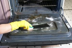 Cleaning the Oven. Hand in glove wiping grime from the oven door.